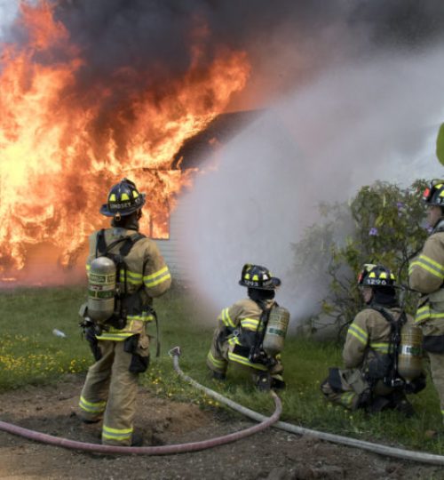 Group of firefighters spraying fire hose at structure.